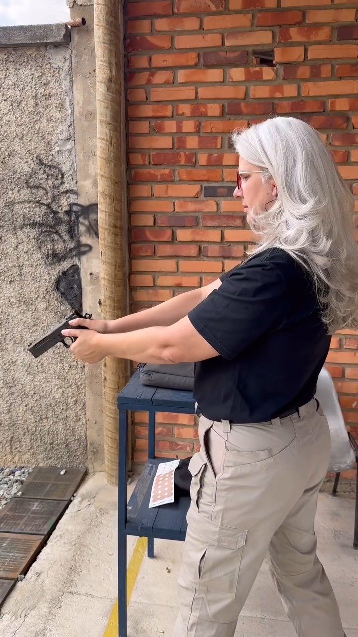 Atiradora pratica com pistola em pista de competição ao ar livre.
