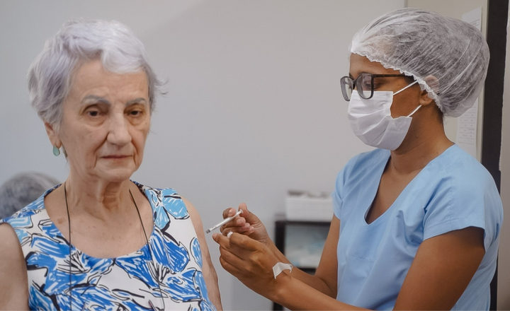 Profissional de saúde aplica vacina no braço de uma mulher idosa.