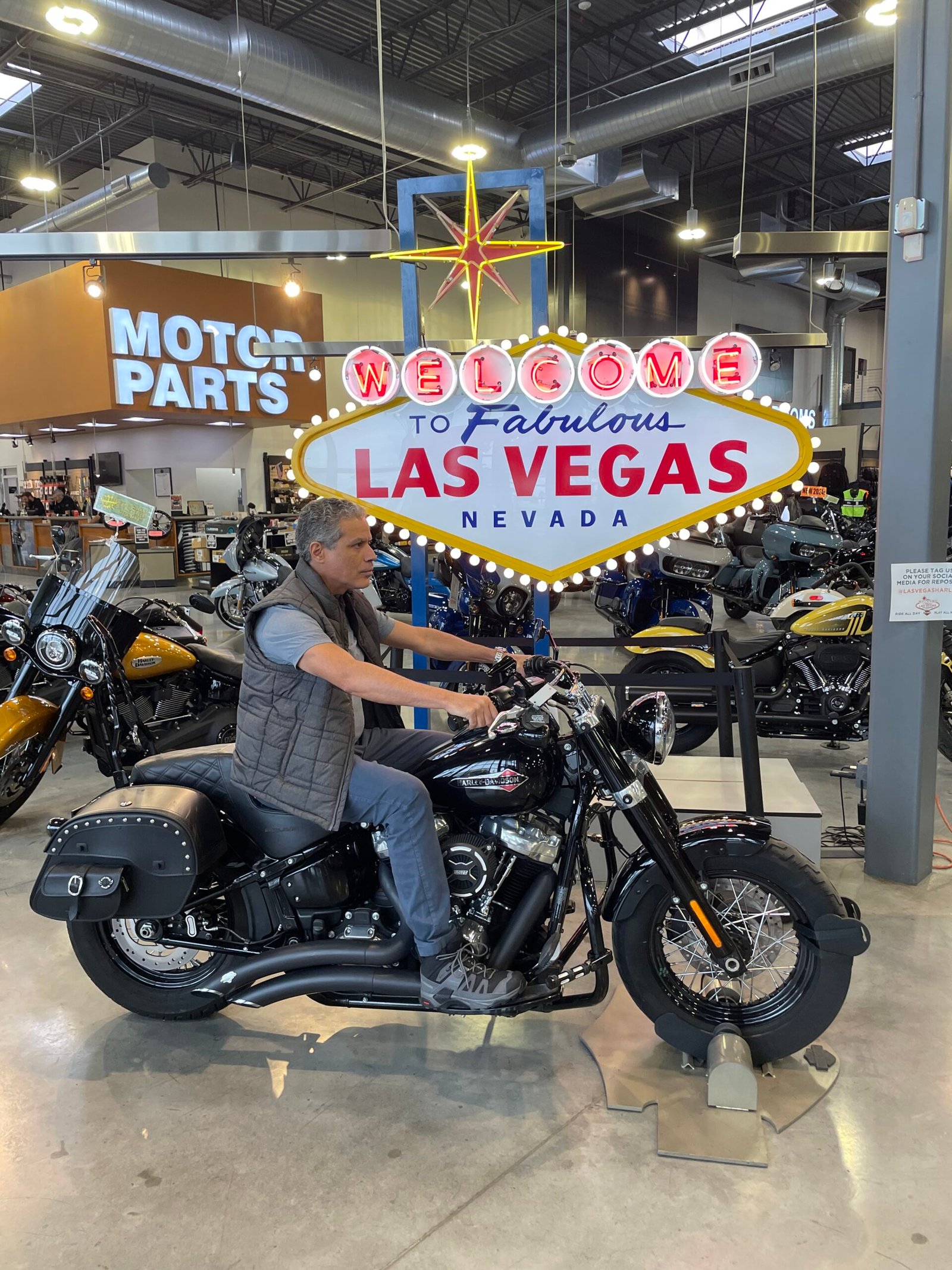Visitante sentado em motocicleta exposta diante de letreiro de Las Vegas.