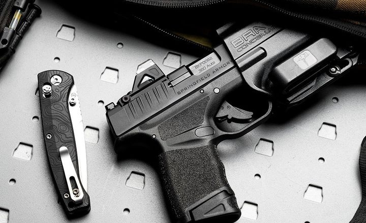 Pistola Springfield Armory Hellcat e canivete sobre superfície metálica.