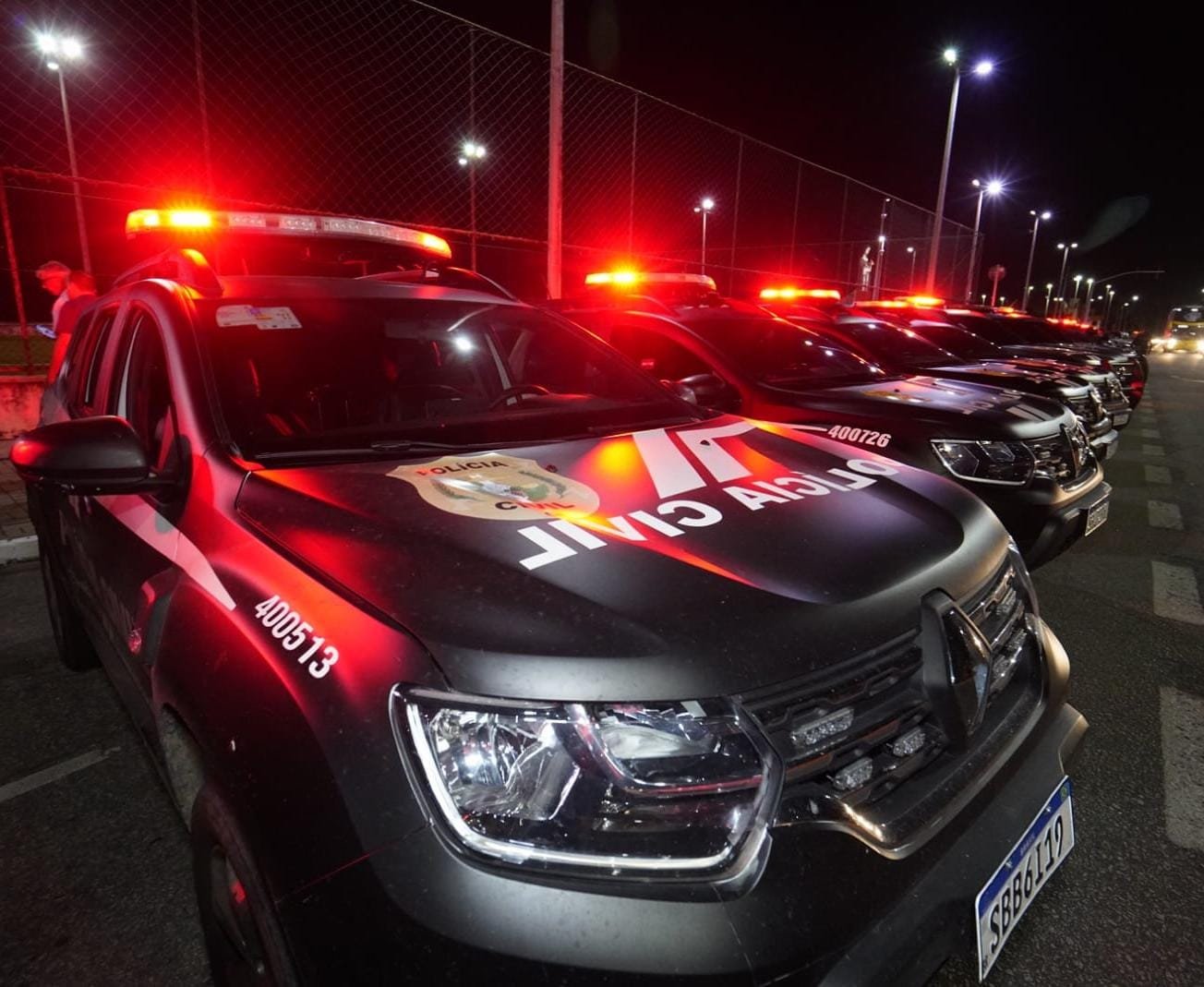 Viaturas da Polícia Civil com luzes vermelhas acesas durante operação noturna.