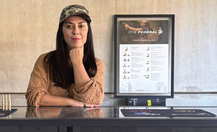 Mulher posa em balcão da Hunterr diante de quadro com componentes de munição.