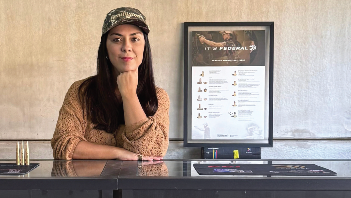 Mulher posa em balcão da Hunterr diante de quadro com componentes de munição.