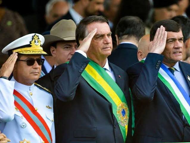 Jair Bolsonaro presta continência usando a faixa presidencial.