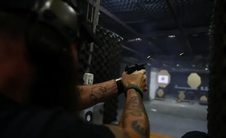 Pessoa dispara uma pistola em um estande de tiro escuro.