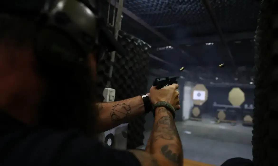 Pessoa dispara uma pistola em um estande de tiro escuro.