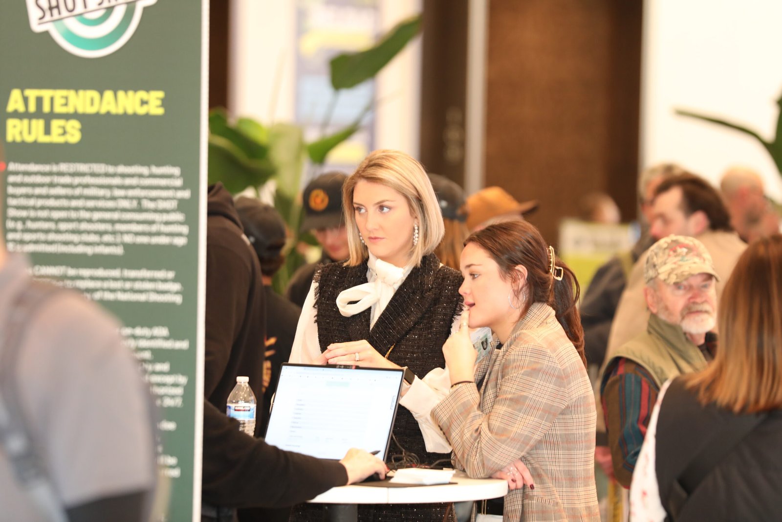 Participantes trabalham em mesas diante do painel de regras de acesso da Shot Show.