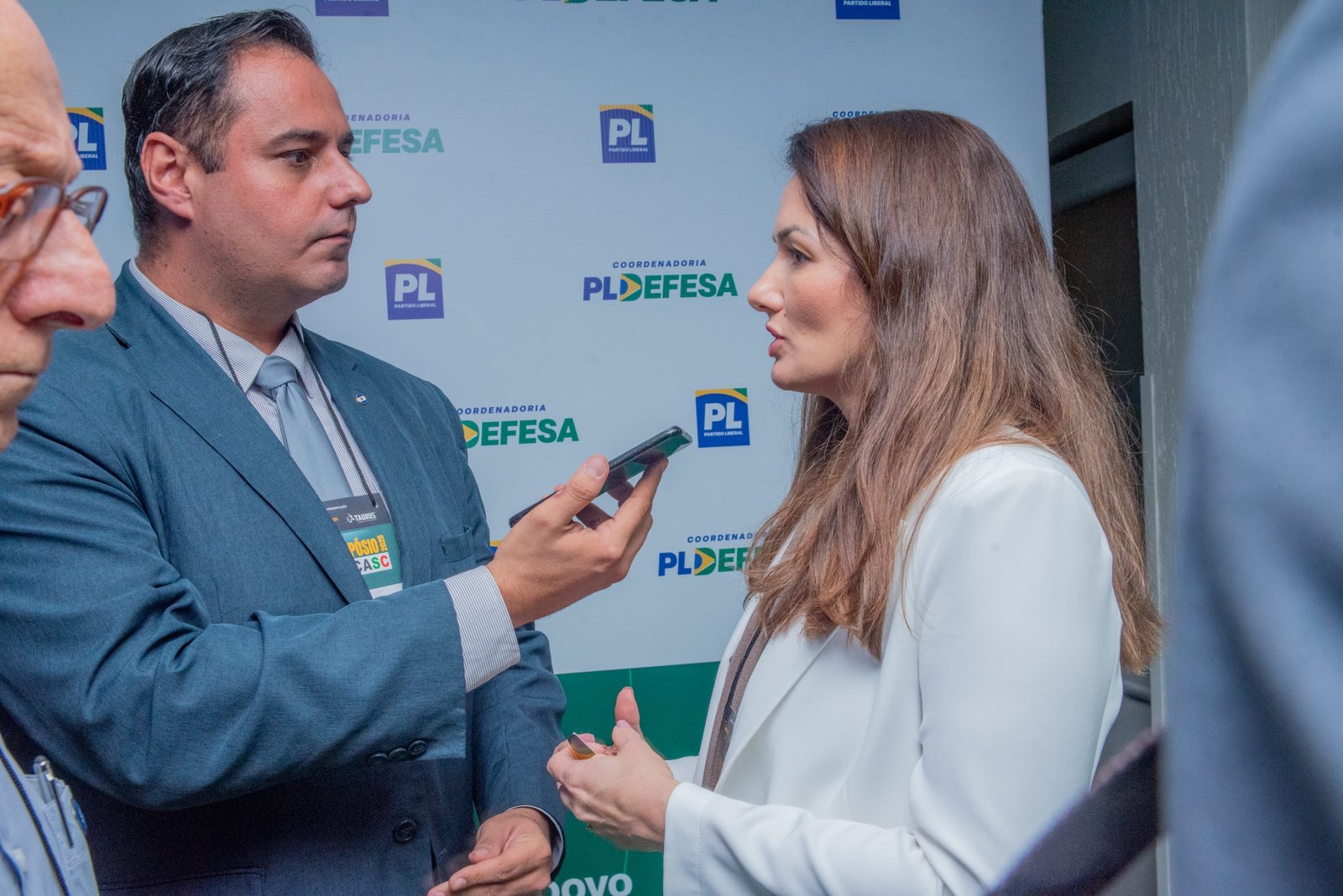 Repórter entrevista participante diante do painel PL Defesa.