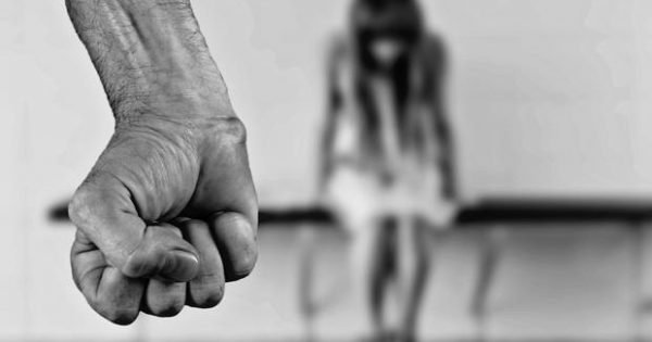 Punho fechado em primeiro plano e silhueta desfocada de adolescente ao fundo.