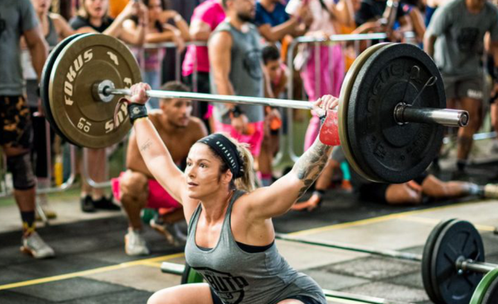 Atleta feminina levanta uma barra com pesos em competição de crossfit.