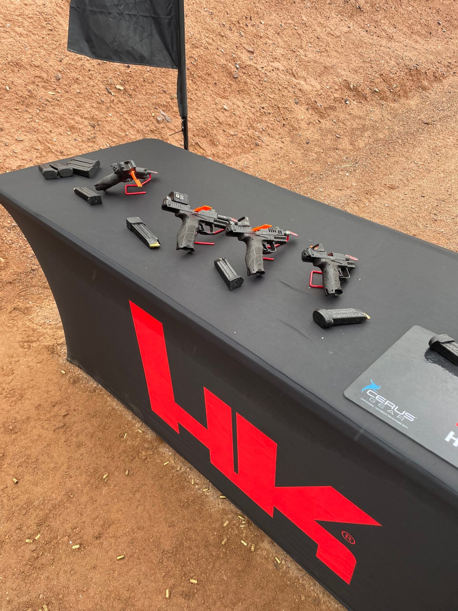Pistolas e acessórios expostos sobre mesa em campo de tiro.
