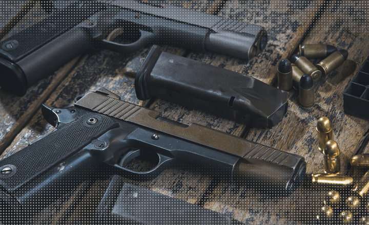 Duas pistolas, carregadores e cartuchos sobre uma bancada de madeira.