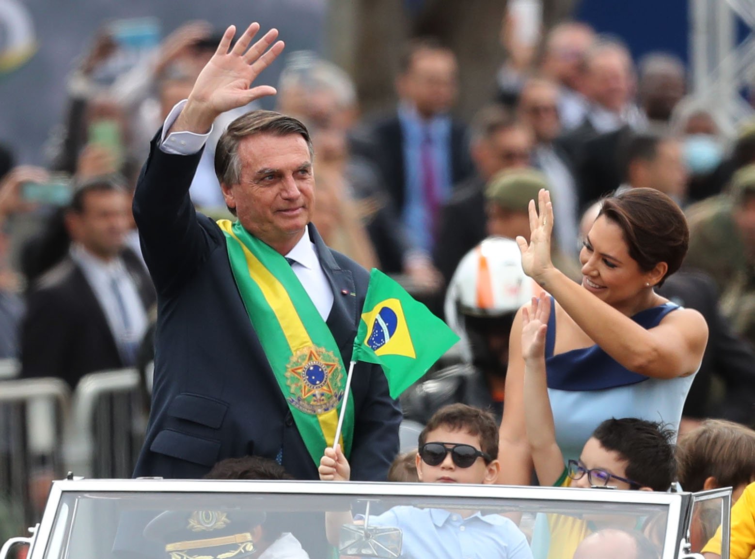 Jair Bolsonaro acena de carro aberto acompanhado da família durante cerimônia.