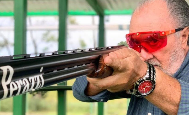 Carlo Danna aponta uma espingarda usando óculos vermelhos de tiro.