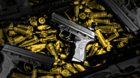 Duas pistolas pretas sobre uma grande quantidade de cartuchos dourados.
