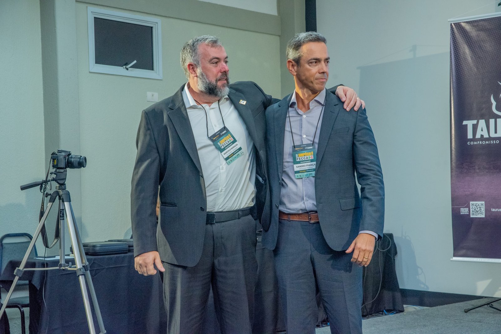 Dois participantes posam juntos em sala do Simpósio FECCASC.