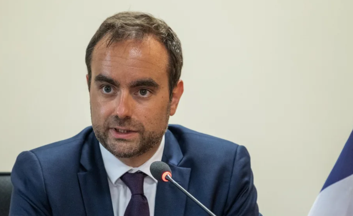 Homem de terno fala ao microfone durante uma reunião oficial.