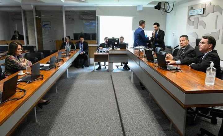 Reunião de comissão com parlamentares e representantes sentados à mesa.