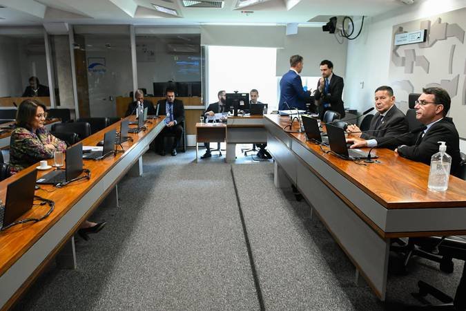 Reunião de comissão com parlamentares e representantes sentados à mesa.
