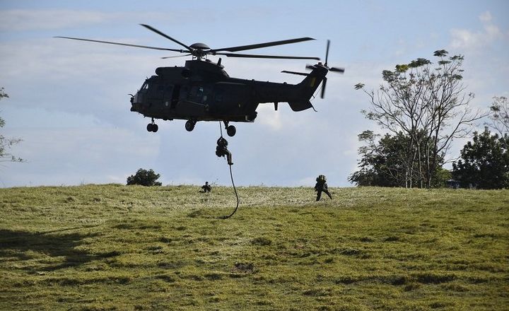 Militar desce por corda de helicóptero durante treinamento em campo.