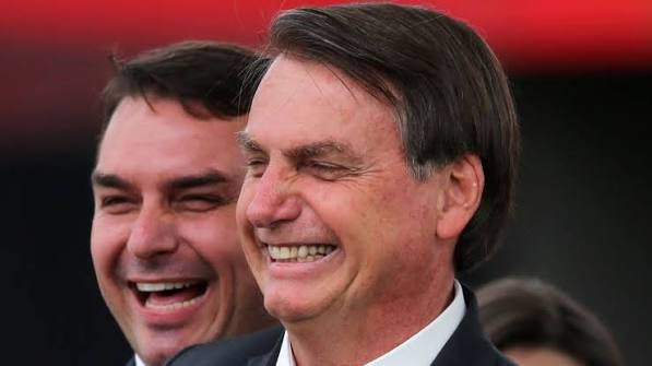 Jair Bolsonaro sorri em primeiro plano durante evento público.